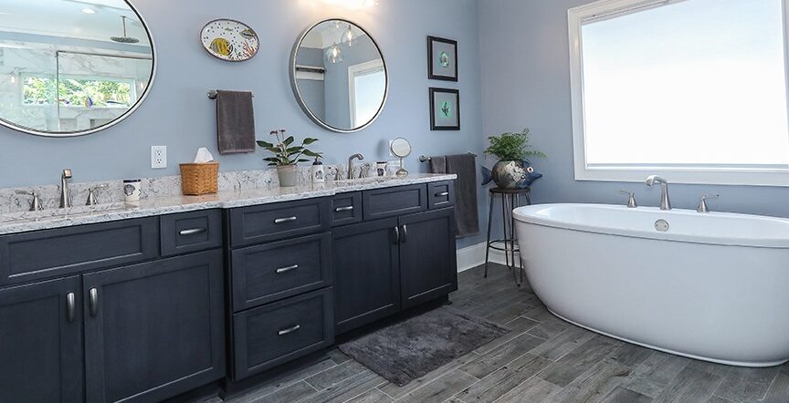Update bathroom with grey tile plank flooring, black cabinetry with grey granite counter tops and a large white tub.