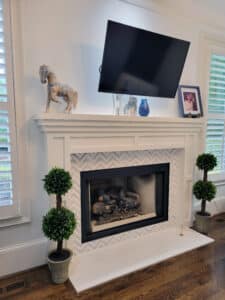 Fireplace with stone hearth, marble chevron pattern surround and wood mantel.